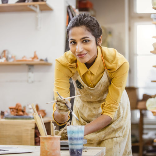 Portrait of a Young Woman Creating Pottery, Using Laptop